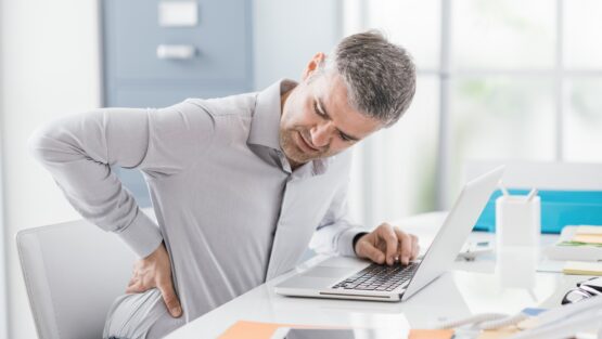Stressed businessman with backache, he is working at office desk and massaging his back