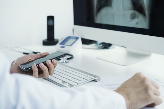 closeup of a young doctor man, wearing a white coat, sitting at his desk checking a chest radiograph in his computer