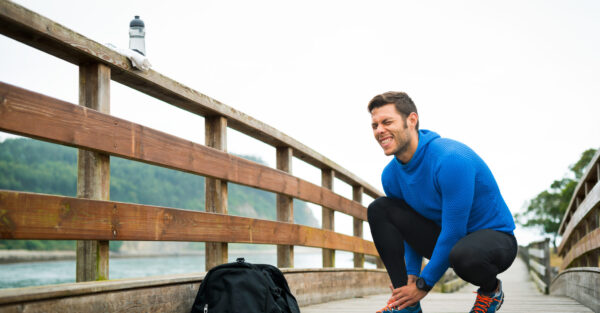 Fit runner sportsman holding ankle in pain in a park. Broken twisted joint running sport injury. Athletic man touching foot due to sprain.